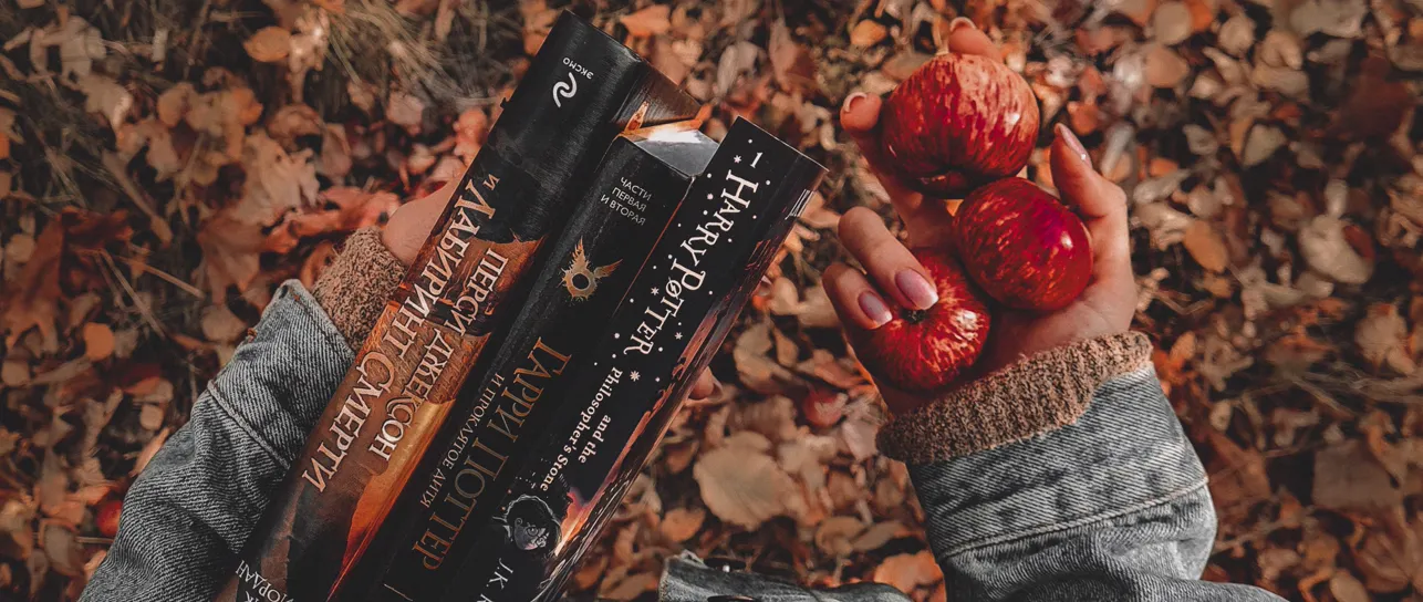 Hands holding books and red apples over autumn leaves